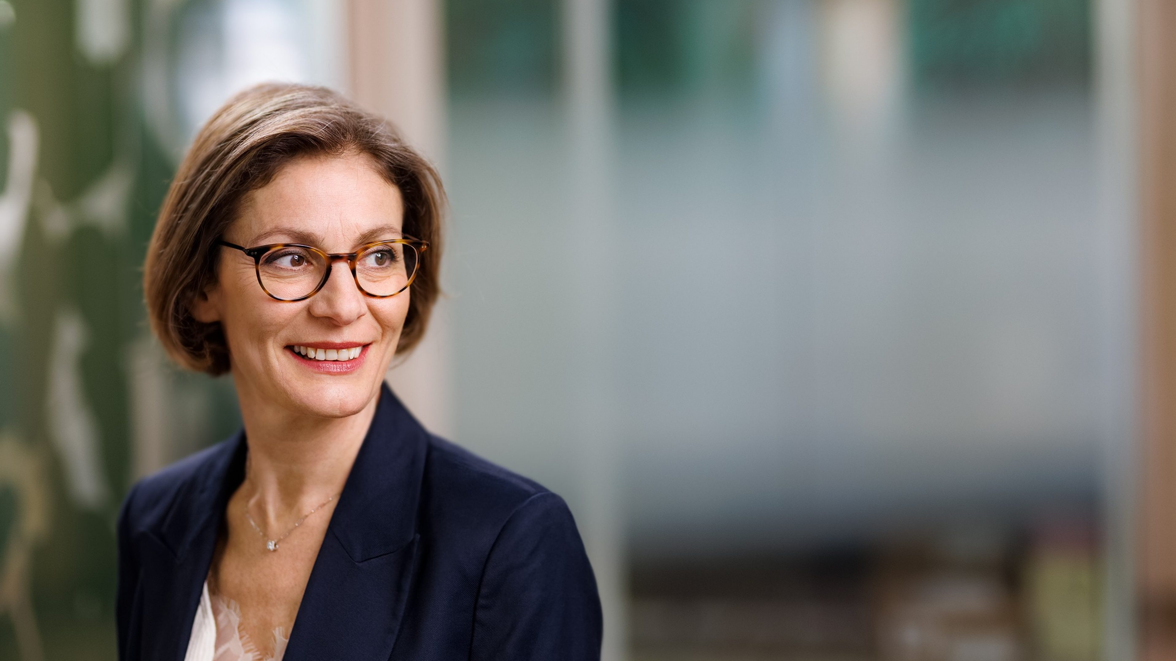 Portrait d'une collaboratrice souriante portant des lunettes, illustrant l'épanouissement professionnel et l'environnement de travail chez Swiss Life Asset Managers.