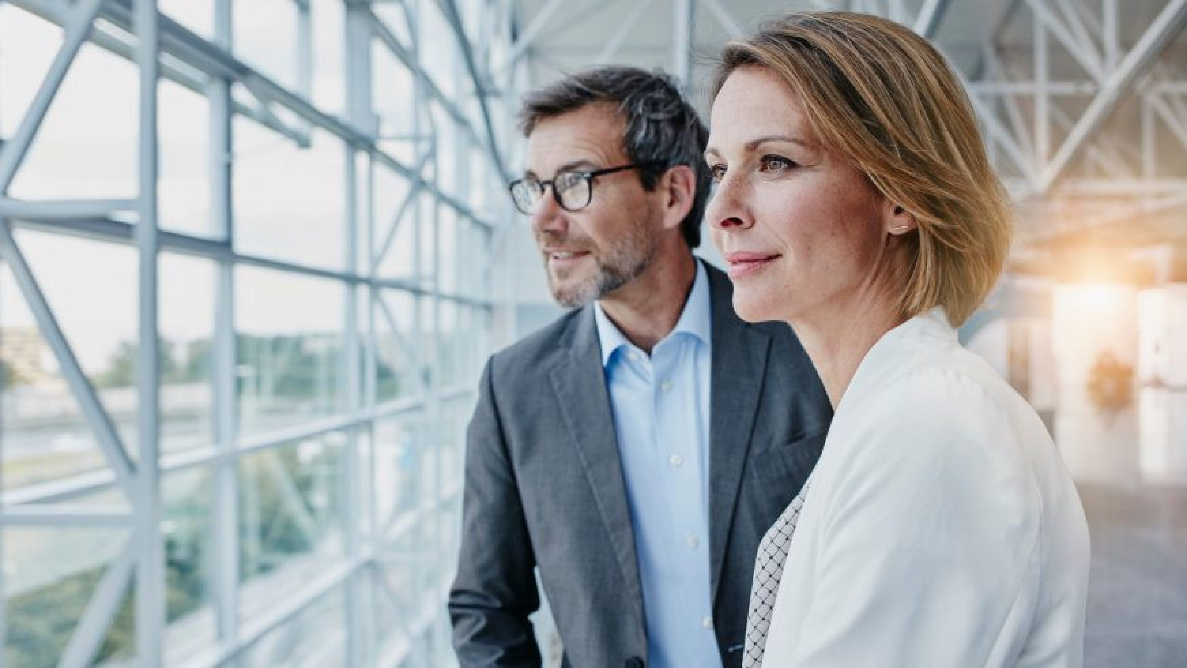Portrait de profil d'une collaboratrice au regard déterminé, travaillant aux côtés d'un collègue dans un environnement de bureau moderne et lumineux.