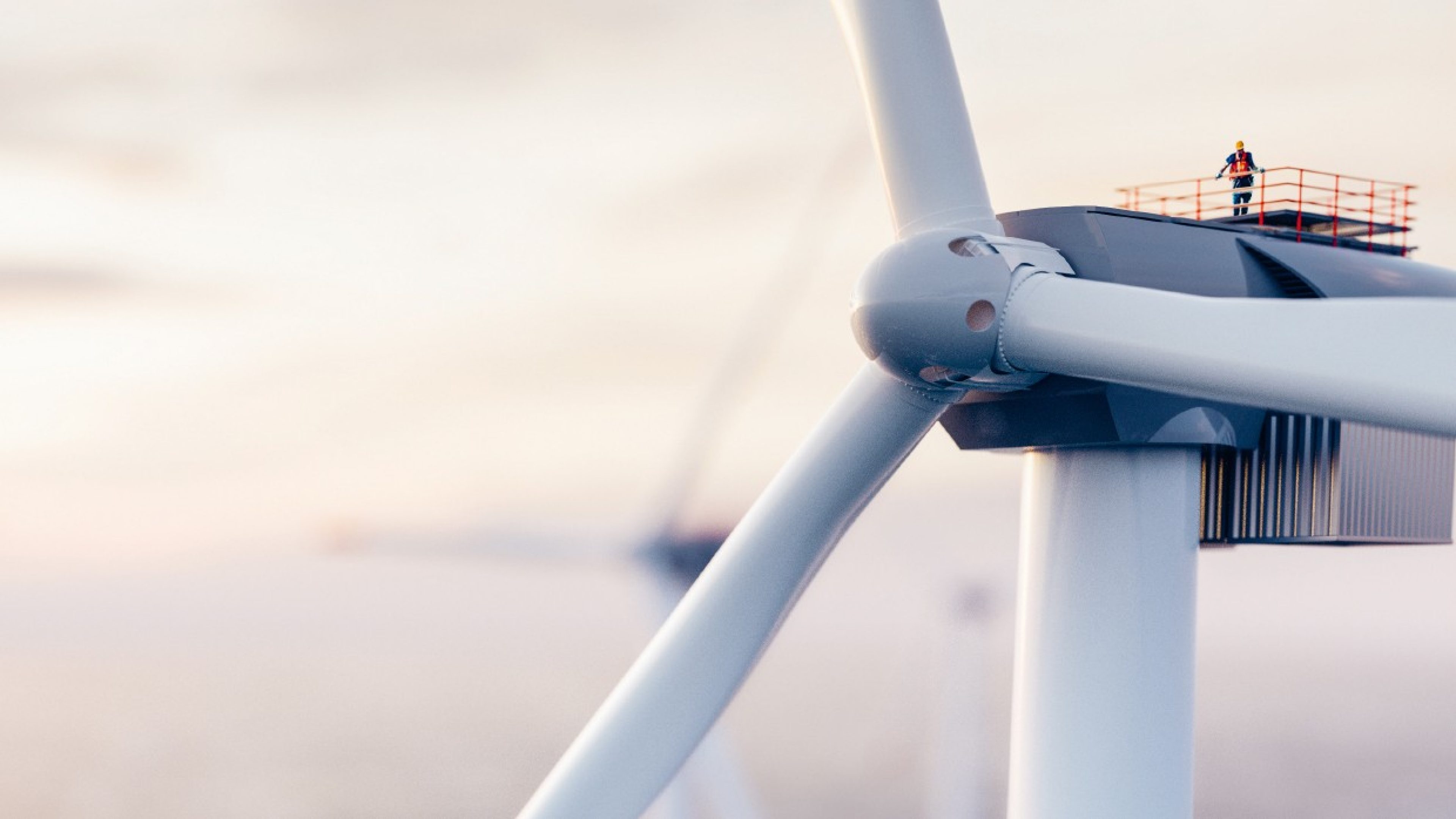 Gros plan sur le moyeu et les pales d'une éolienne blanche sur un fond de ciel clair au lever du jour.