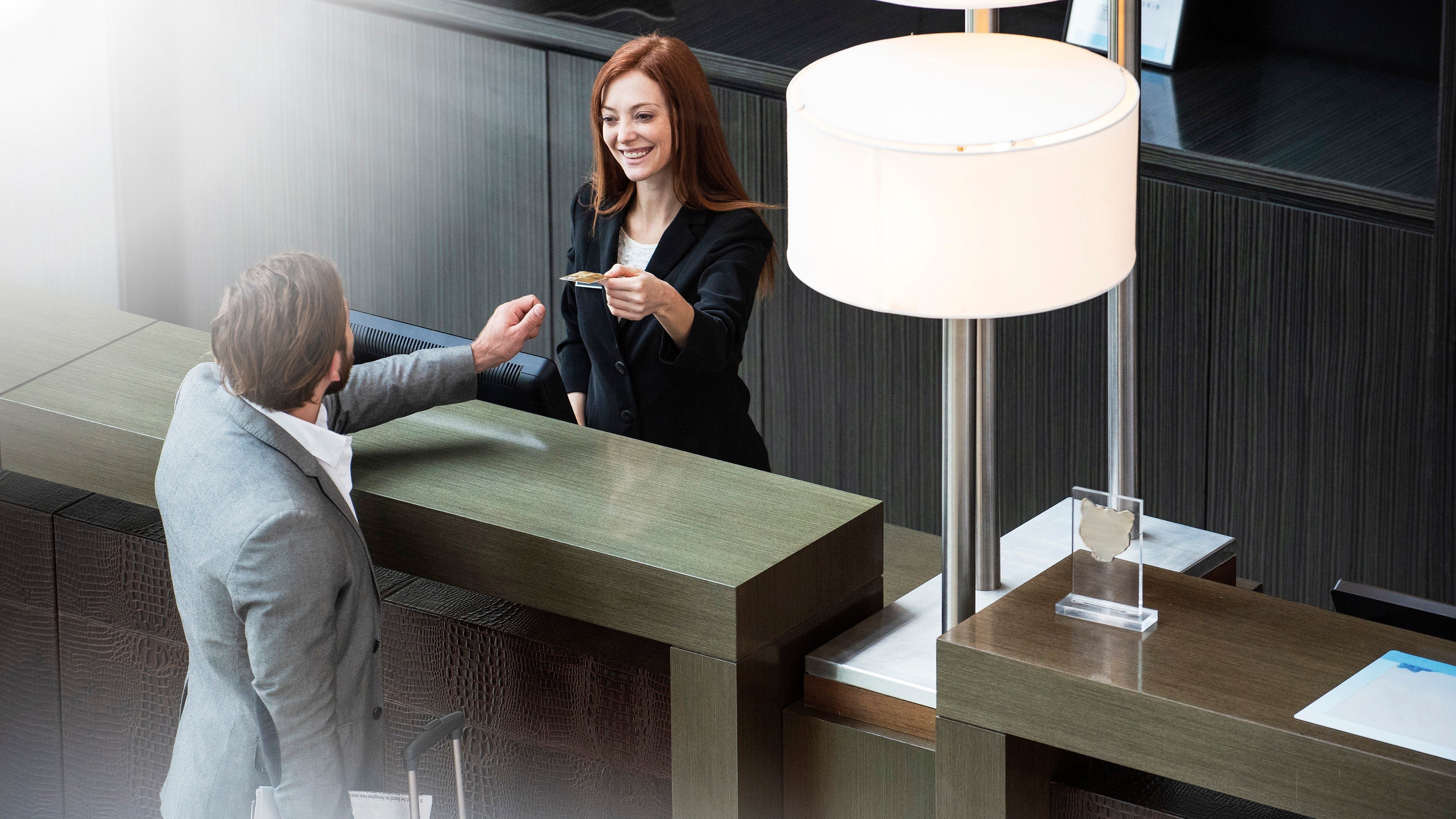 Réceptionniste souriante accueillant un client à la banque d'accueil d'un hôtel moderne et élégant.