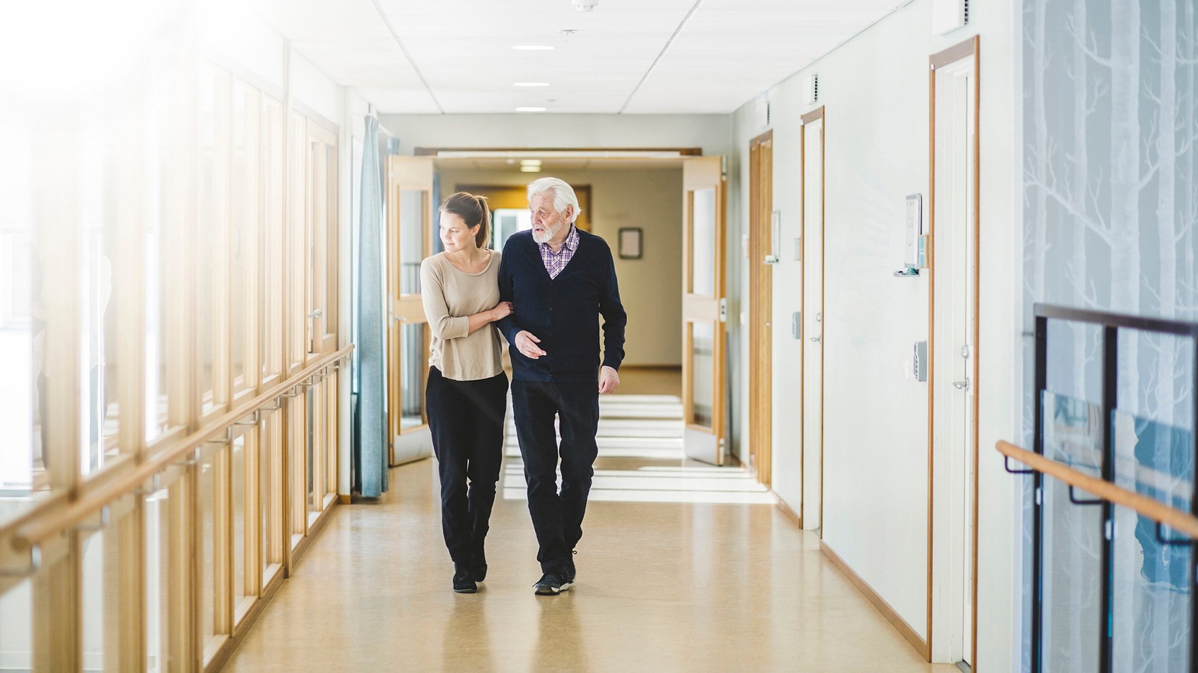 Couloir d’établissement de santé avec accompagnement d’une personne âgée
