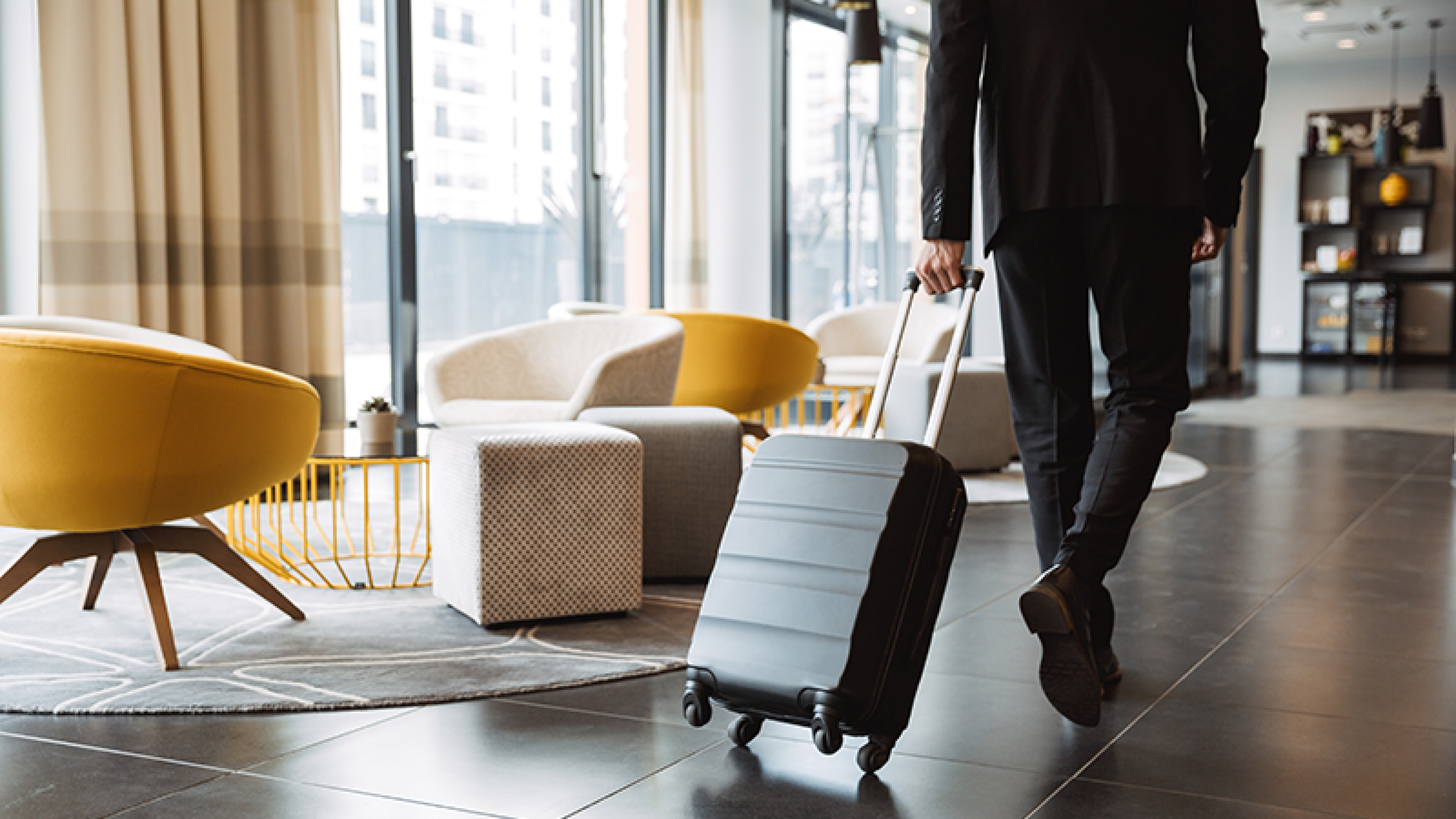 Intérieur d’un hôtel moderne avec un voyageur tirant une valise à roulettes dans le hall, illustrant le secteur de l’hôtellerie.