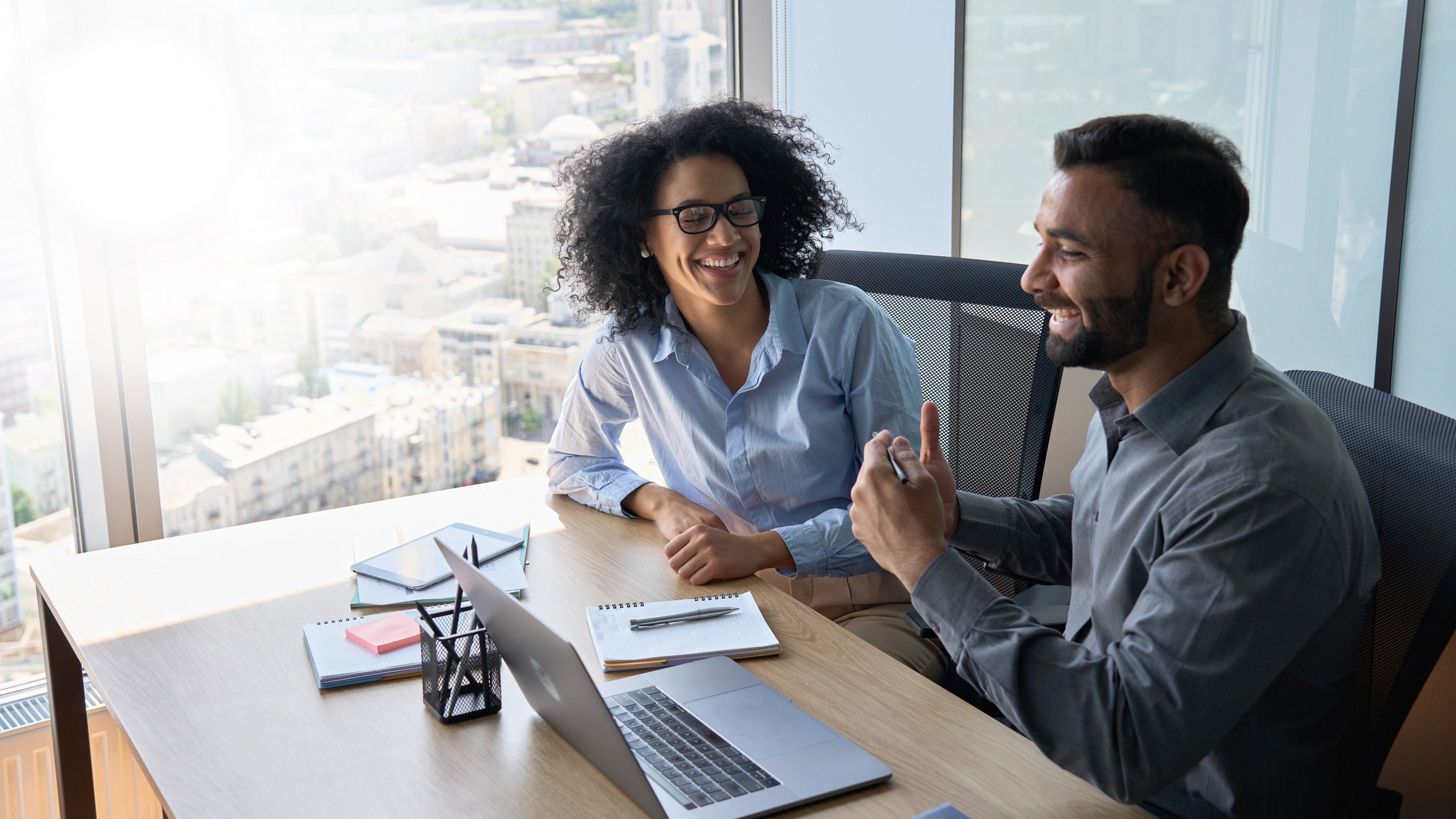 Un homme et une femme en réunion dans un bureau lumineux, souriant et échangeant autour d'un ordinateur portable.