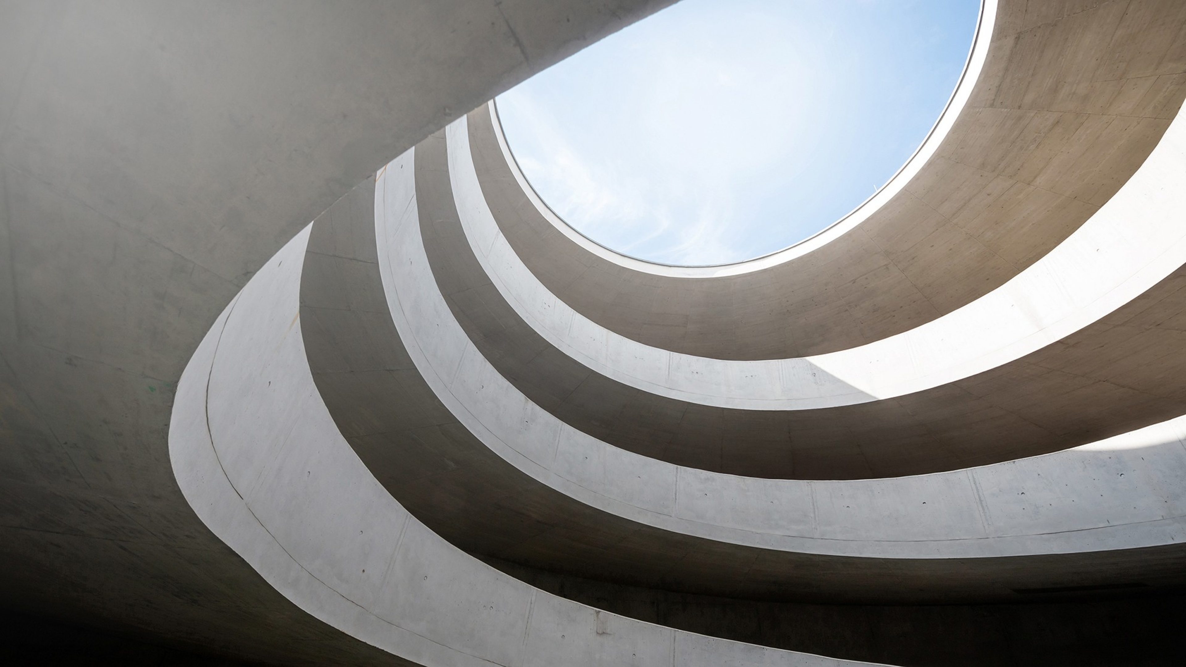 Photographie d'un escalier en colimaçon moderne vue du dessous, créant une spirale architecturale vers le ciel.