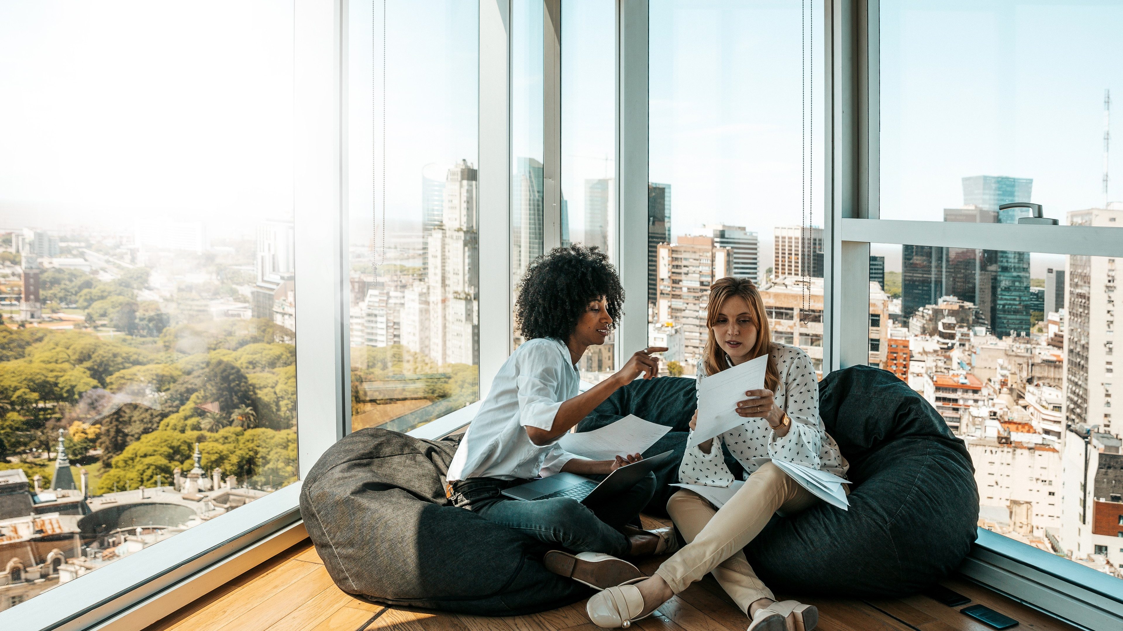 Deux collaboratrices travaillant ensemble dans un bureau moderne avec une vue panoramique sur la ville.