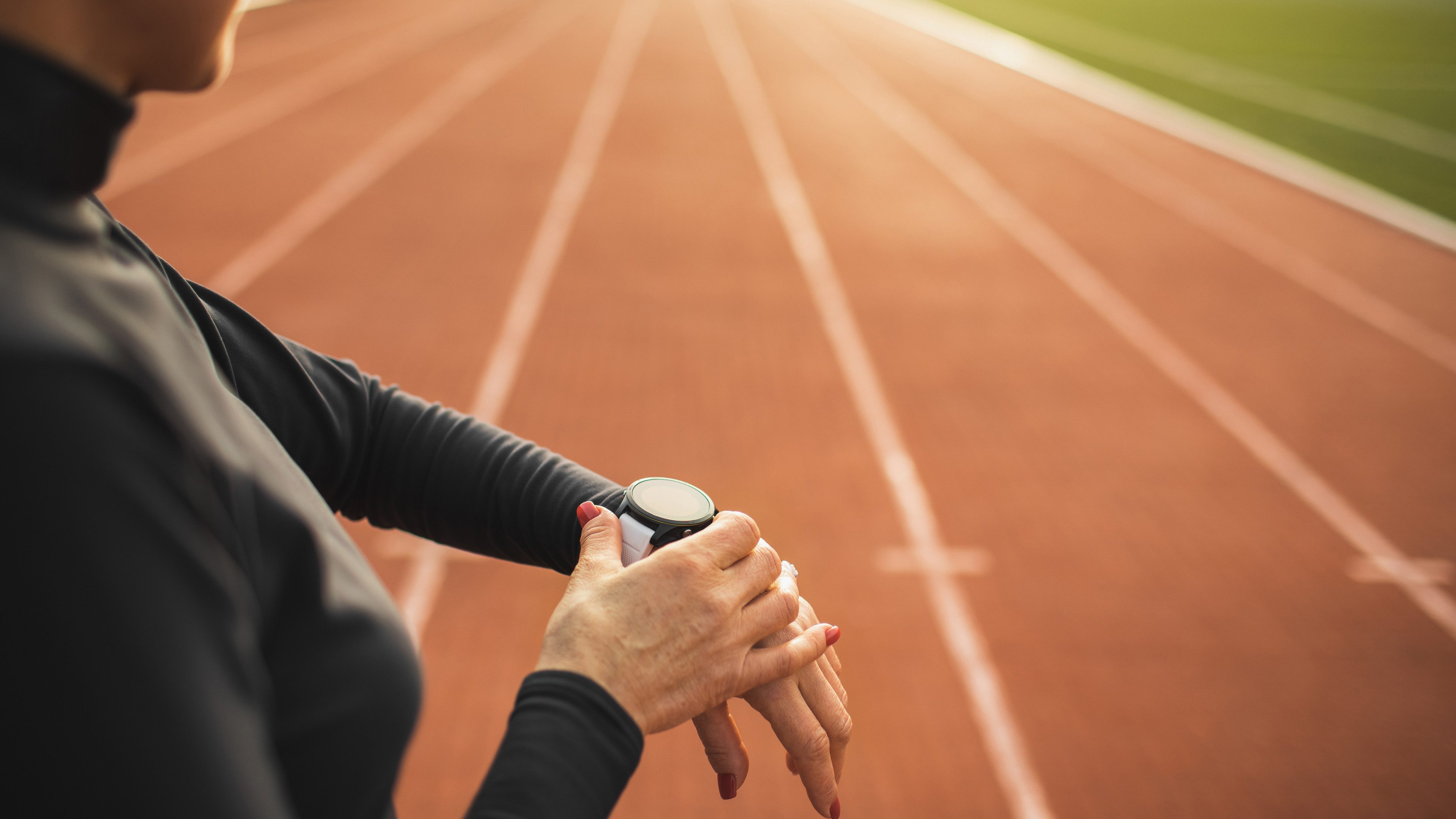 Gros plan sur une personne réglant sa montre connectée sur une piste d'athlétisme.