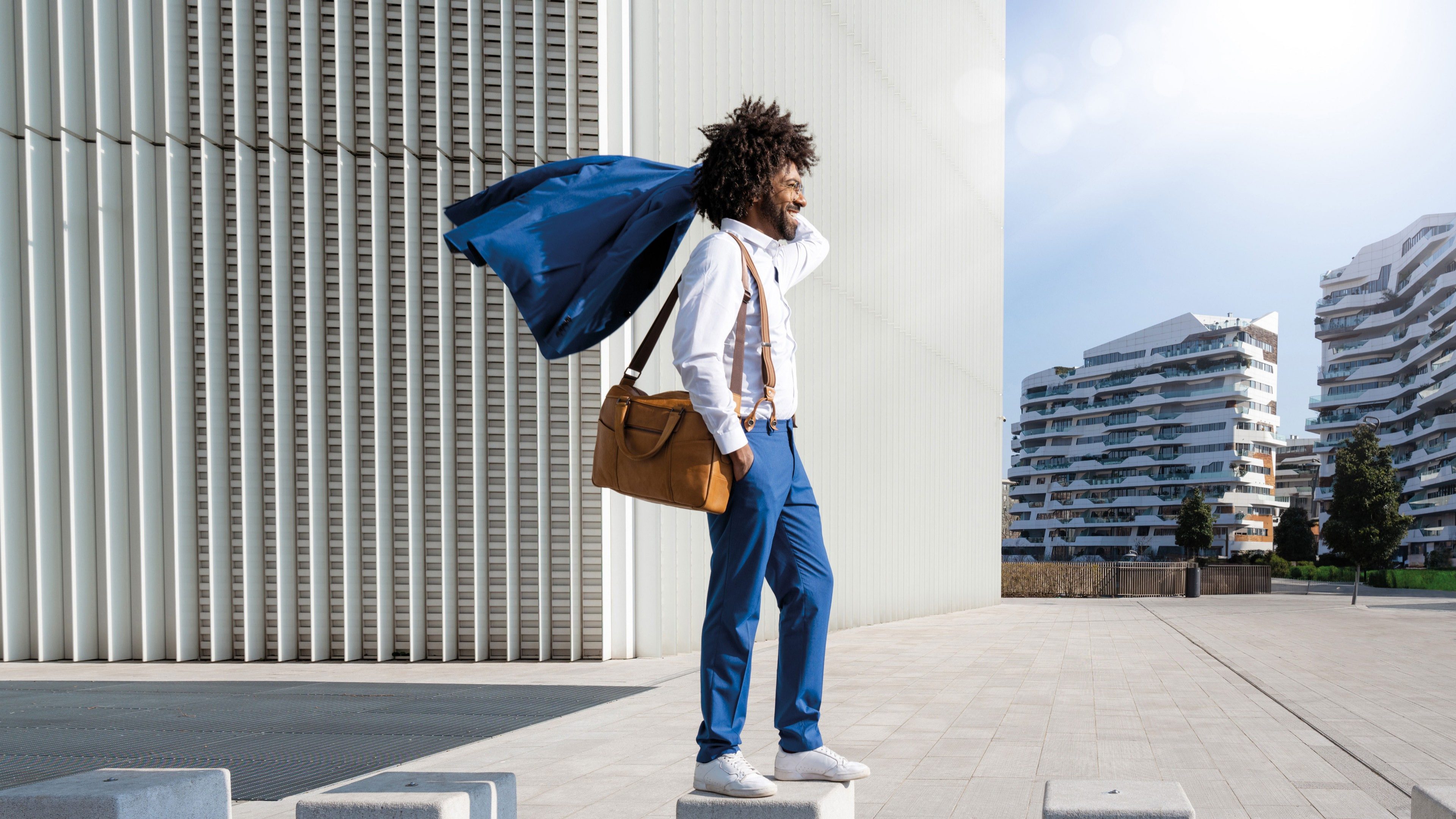 Homme marchant dans une rue moderne avec un sac sur l'épaule, symbolisant la mobilité urbaine.
